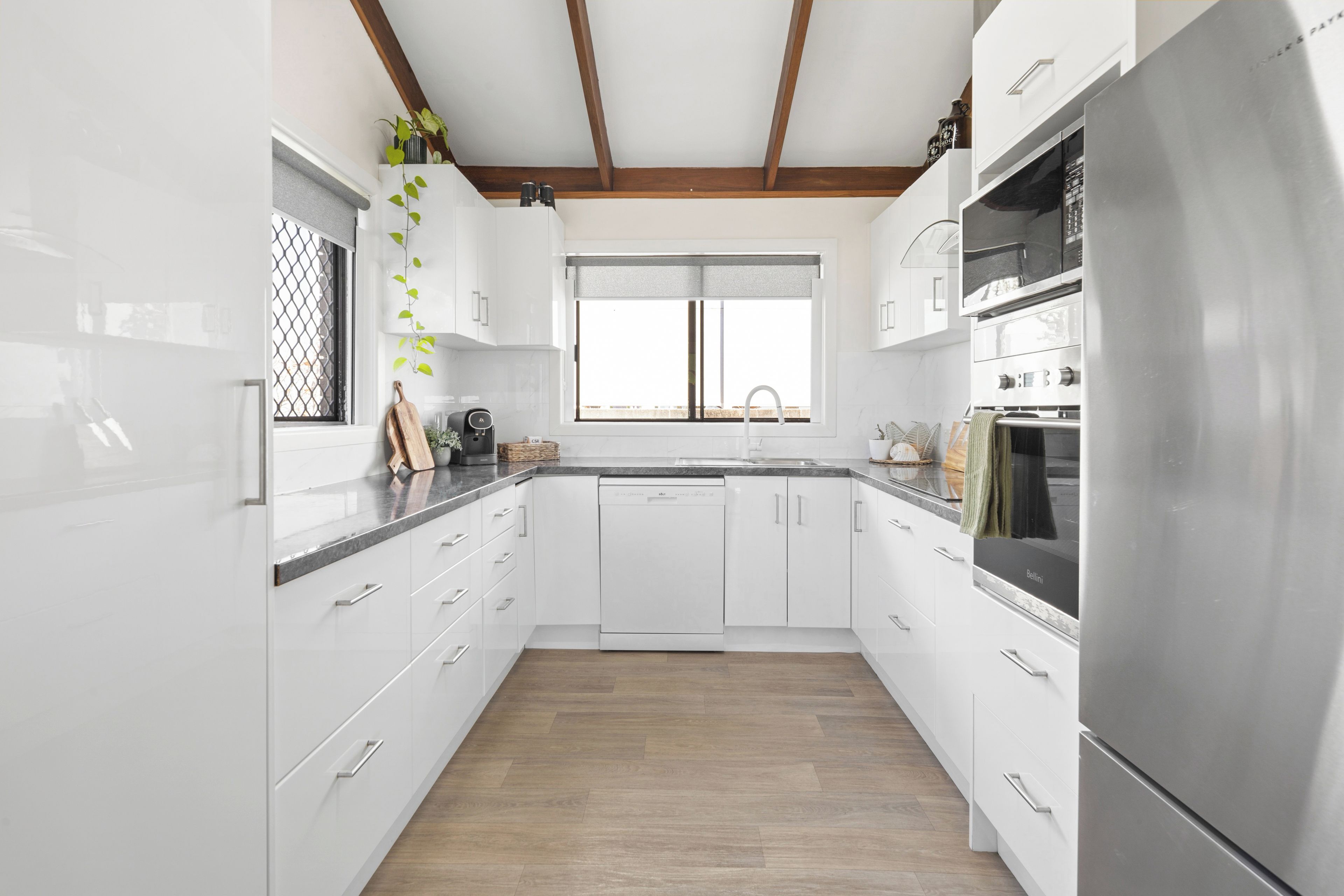 A modern kitchen with white cabinetry, a stainless steel refrigerator, and a window above the sink.