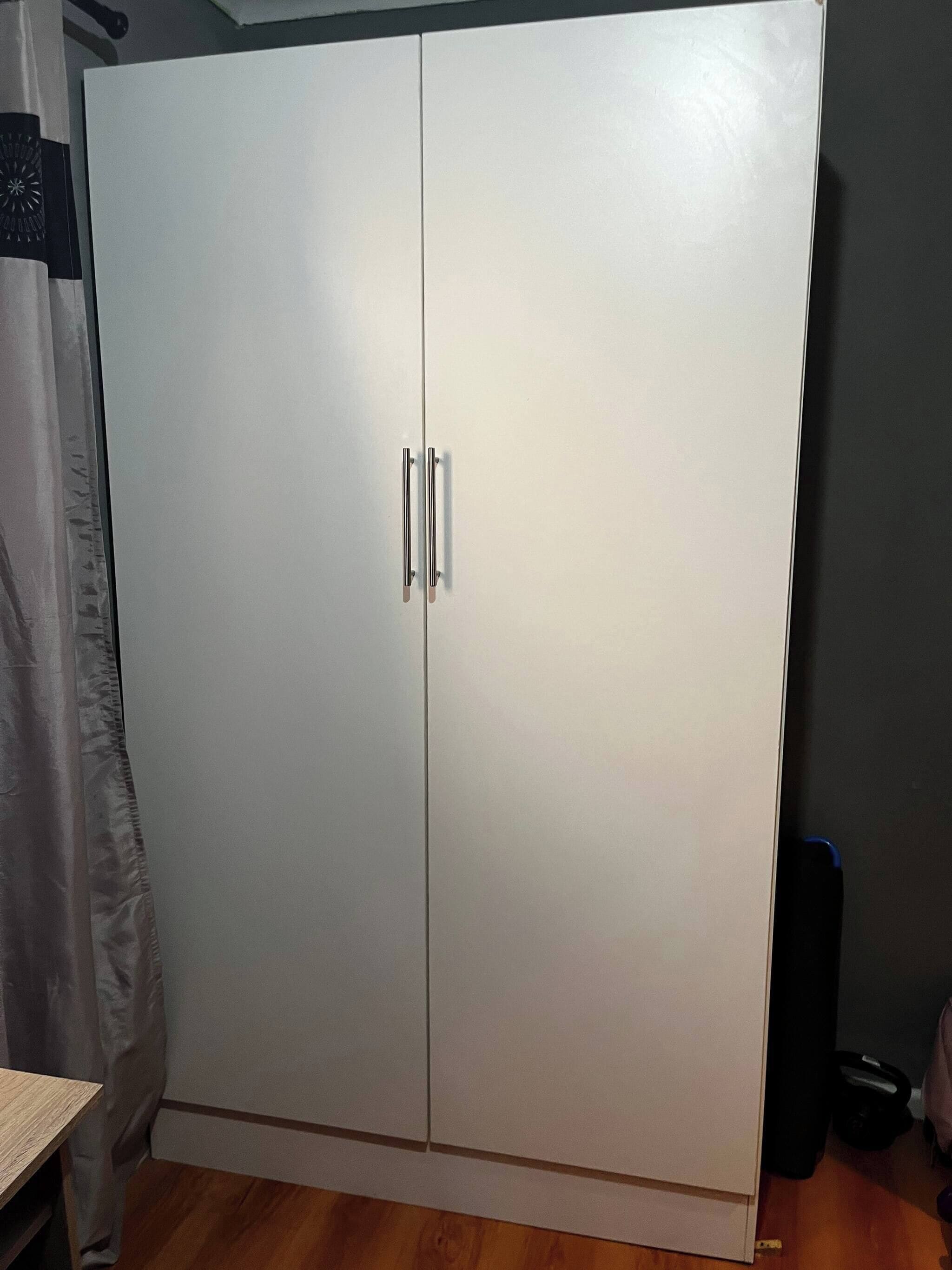 A large wardrobe with two doors and handles, a wooden floor, and a curtain partially visible.
