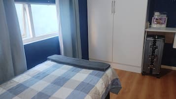 Et soveværelse med en seng, et garderobeskab, en hylde med toiletartikler og et vindue med persienner.