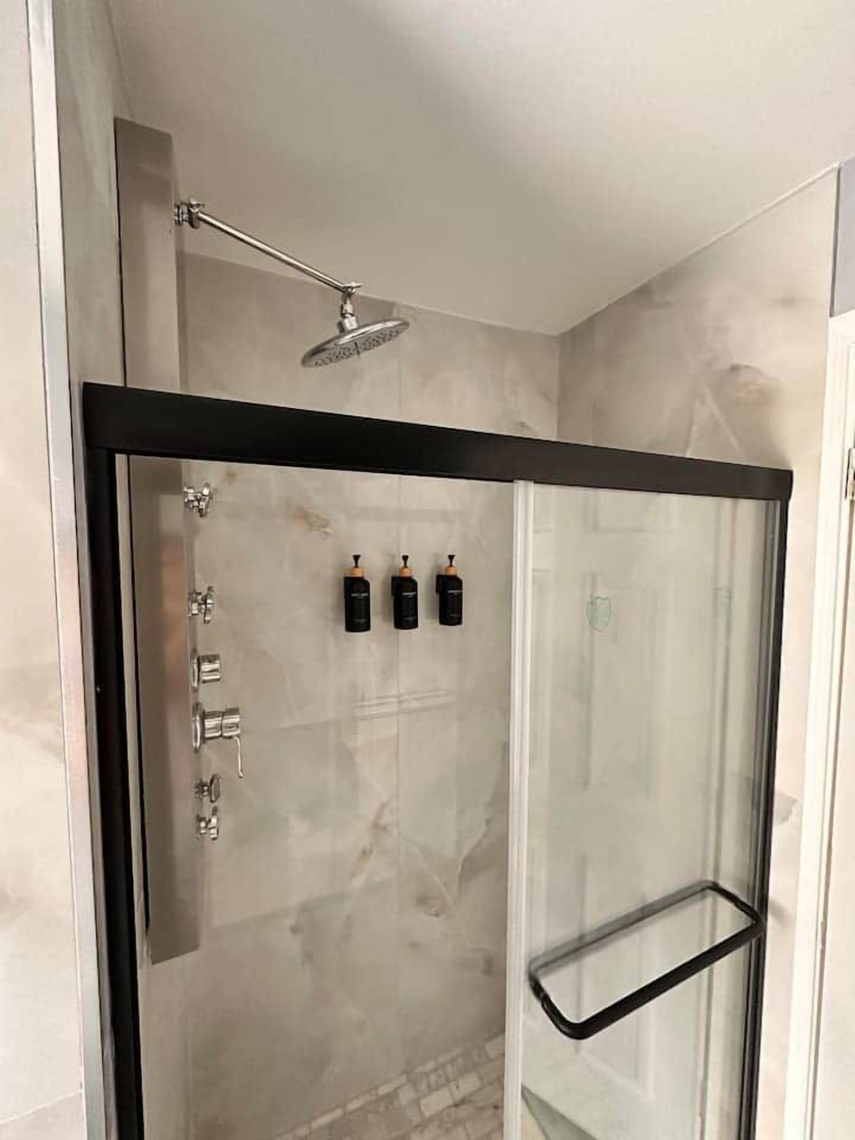 Ducha con mampara de vidrio, cabezal de ducha de mano, puerta de vidrio y toallero negro.