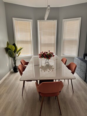 A dining area with a marble table, six chairs, a vase with flowers, and a potted plant.