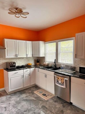 A kitchen with white cabinets, a black countertop, a stainless steel dishwasher, and a window with blinds. - Brand New Stunning Home 3 min to Niagara Falls (Niagara Falls)