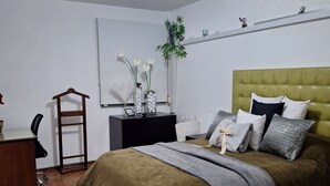 Een slaapkamer met een bed, nachtkastje, lamp en een hangplant.