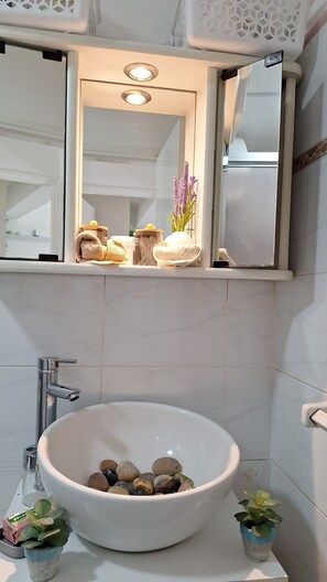 Un baño con un lavabo blanco, un espejo encima y una ventana con vistas al exterior.