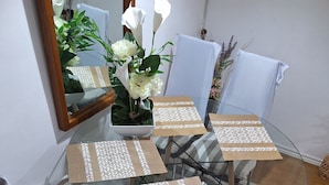 A dining area with a glass table, striped rug, and white chairs.