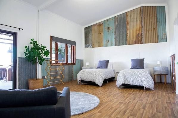 A modern bedroom with two beds, a large window, a plant, and a wooden floor.