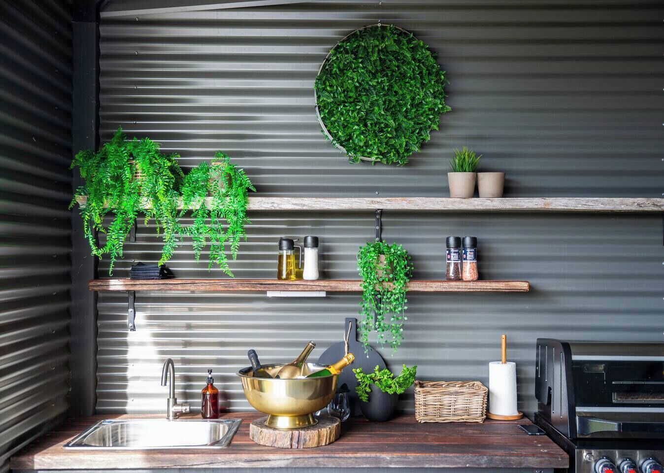 A kitchen with a sink, a stove, and various kitchen utensils. There are also several potted plants and a round green wall hanging.