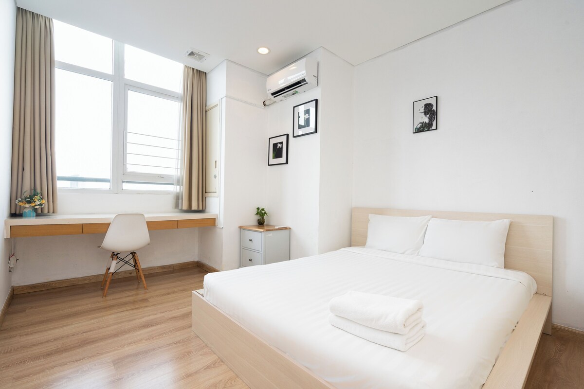 A modern hotel room with a large bed, a desk, and a window with curtains.