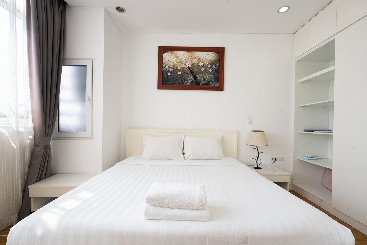 A hotel room with a bed, a nightstand, a lamp, a painting, and a wardrobe.