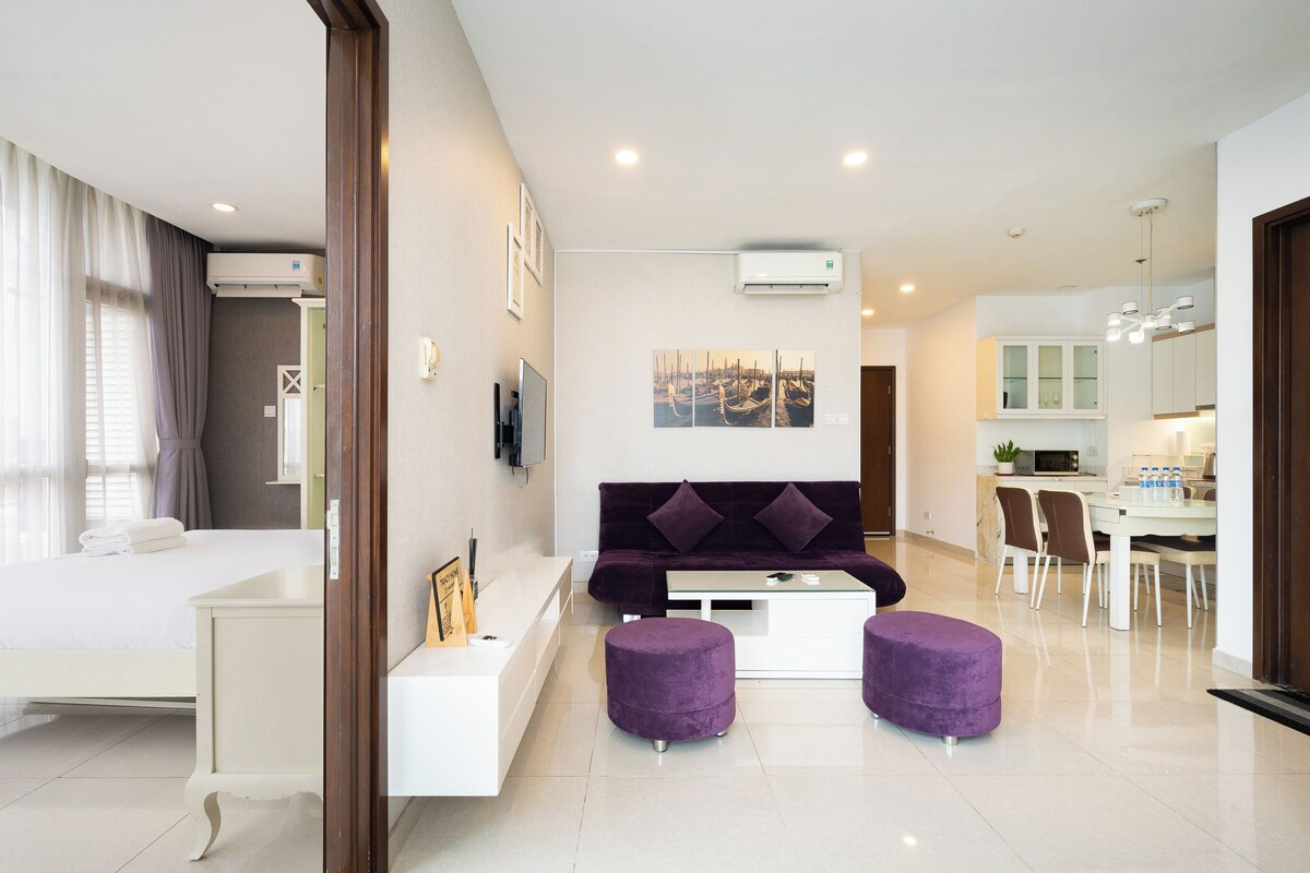 A modern living room with a sofa, ottomans, a coffee table, and a dining area with chairs and a table.