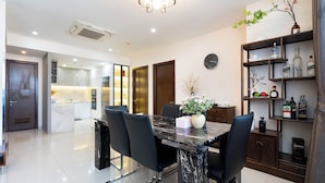 A modern dining area with a marble table, black chairs, a chandelier, and a wall-mounted clock. - IMPERIAL JADE SUITE at THE ONE SAIGON (Ho Chi Minh City)