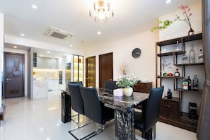 A modern dining area with a marble table, black chairs, a chandelier, and a wall-mounted clock. - IMPERIAL JADE SUITE at THE ONE SAIGON (Ho Chi Minh City)