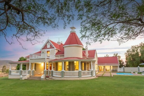 A large house with a red roof, multiple balconies, and a swimming pool. - Ostrich Baron's Palace (Oudtshoorn)