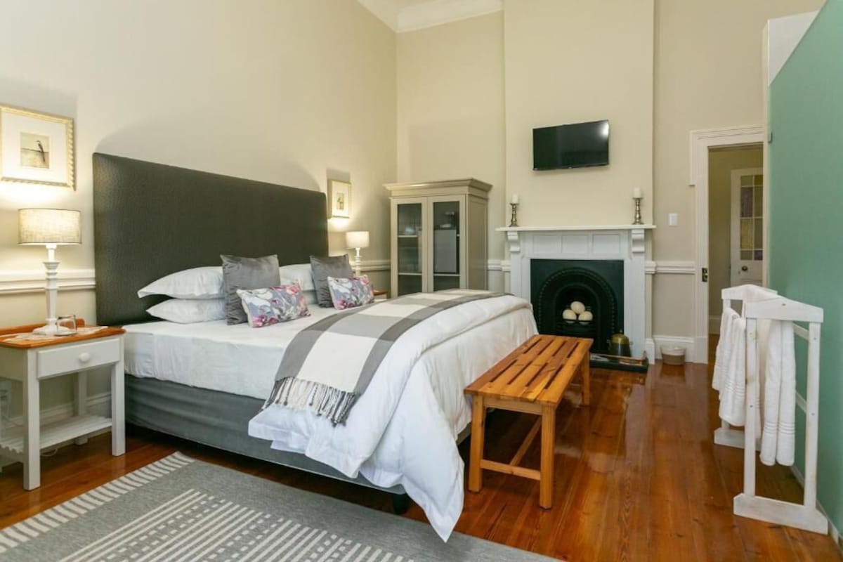 A bedroom with a bed, bedside table, lamp, and a fireplace.