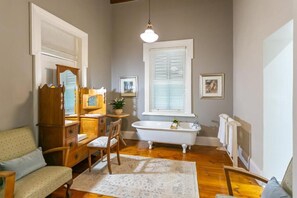 A bathroom with a bathtub, wooden furniture, a mirror, and framed pictures on the wall. - Ostrich Baron's Palace (Oudtshoorn)