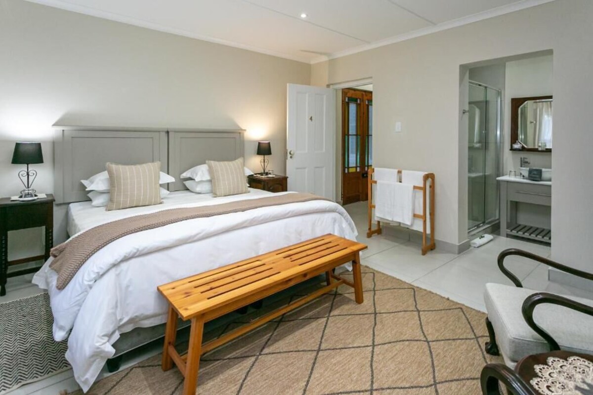 A bedroom with a bed, bedside tables, a bench, a chair, a bathroom with a shower, and a mirror.