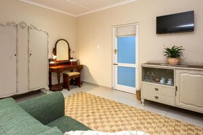 A room with a green sofa, a wooden desk with a mirror, a television, and a cabinet with glass doors. - Ostrich Baron's Palace (Oudtshoorn)