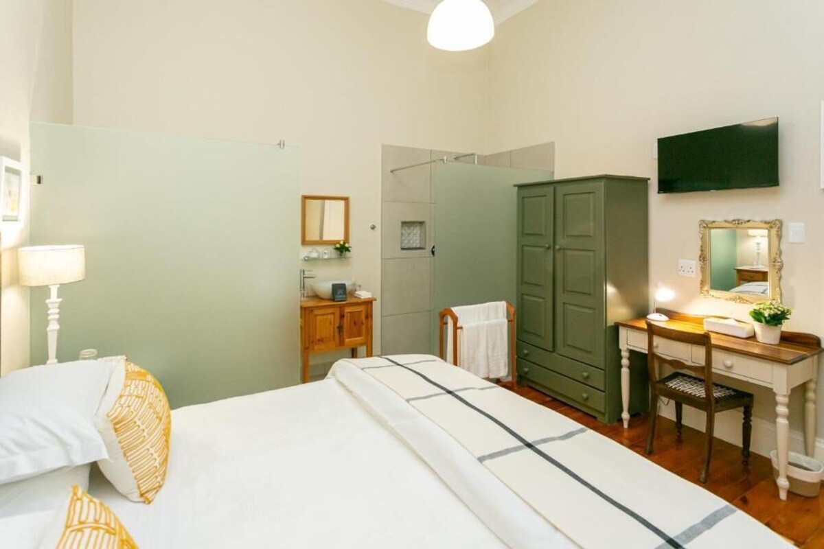 A hotel room with a bed, a desk with a chair, a wardrobe, a mirror, and a television.