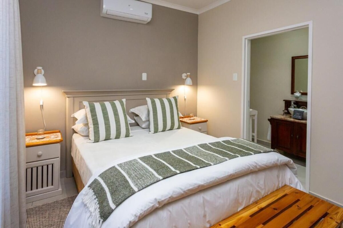 A bedroom with a bed, bedside tables, a lamp, a mirror, and a wooden bench.
