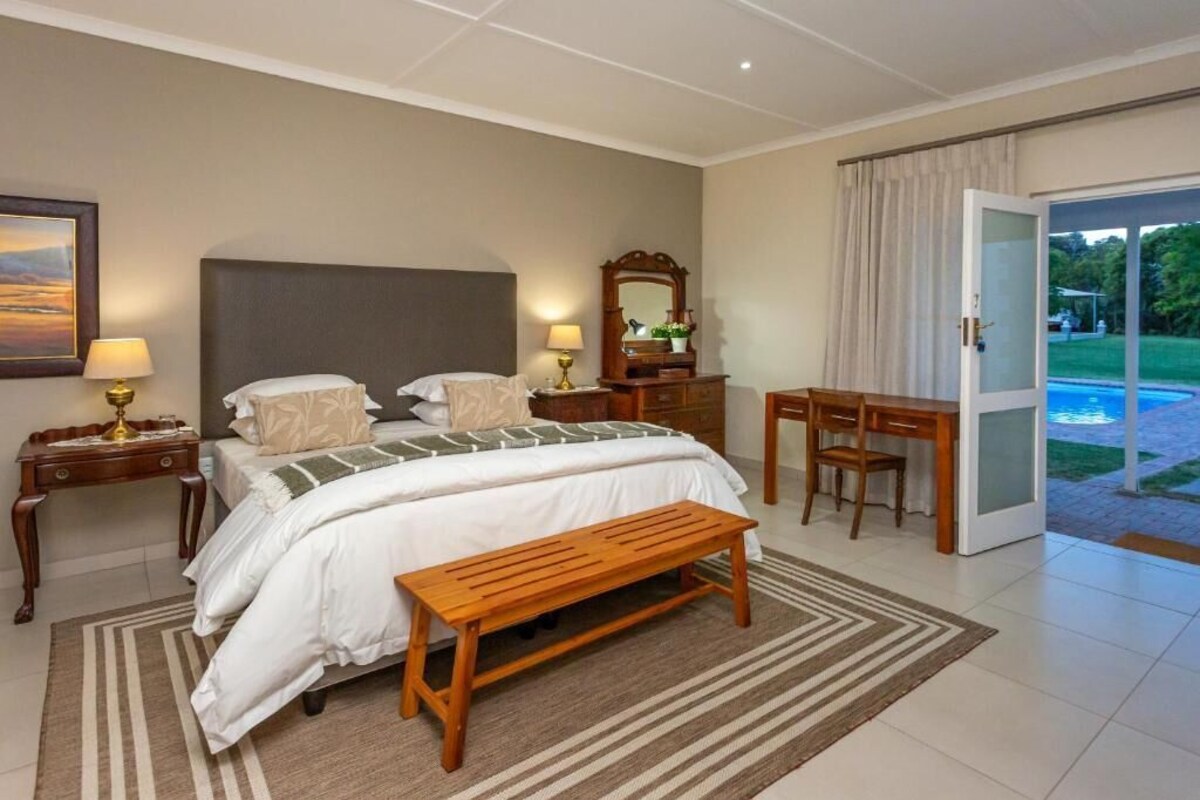 A bedroom with a bed, bedside tables, a bench, a desk, and a view of a swimming pool.