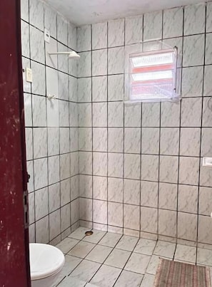 A bathroom with a white toilet, a shower with a window, and tiled walls. - Studio apartment for two people near Praia do Amor (Tibau do Sul)