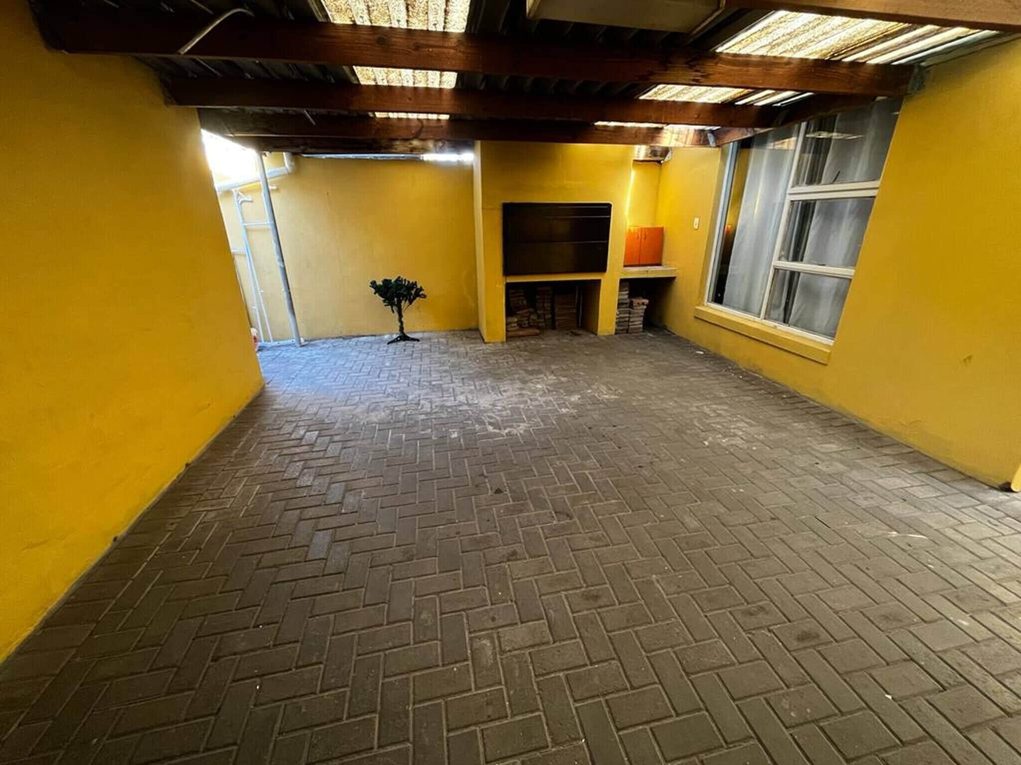 Ett rum med ett tegelgolv, synliga träbjälkar i taket och gula väggar.