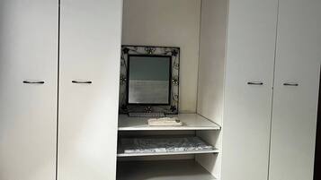Un armario blanco con espejo y repisas, un teclado y una computadora portátil sobre la repisa superior.
