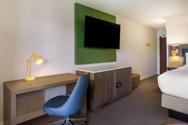 Ein Hotelzimmer mit Schreibtisch, blauem Sessel, Fernseher an einer grünen Wand und einem Bett.