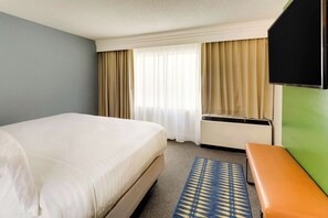 Ein Hotelzimmer mit einem großen Bett, einer Bank, einem Flachbildfernseher und einem Fenster mit Vorhängen.