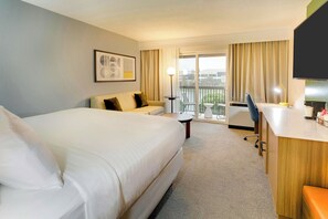 Ein Hotelzimmer mit einem großen Bett, einem Sofa, einem Schreibtisch mit Stuhl, einem Fernseher und einem Balkon mit Tisch und Stühlen.