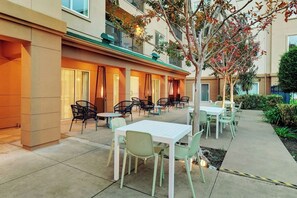 Eine Außenpatio-Terrasse mit Tischen, Stühlen, einem Baum und einem Gebäude mit Balkonen.