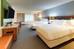 Ein Hotelzimmer mit zwei Betten, einem Schreibtisch, einem Fernseher und einer Sitzecke.