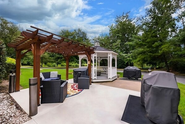Ein überdachter Patio-Bereich mit Gartenmöbeln, einer Laube und einem Grill.