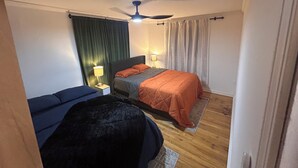 A hotel room with a bed, a nightstand, a lamp, a ceiling fan, and a window with curtains.
