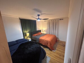 A hotel room with a bed, a nightstand, a lamp, a ceiling fan, and a window with curtains.