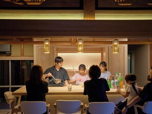 A group of people seated at a counter with a chef preparing food, in a room with wooden paneling and pendant lighting. - Imagasa-so, Nara, Kitamachi - Manaka no Yu - (奈良市押小路町)