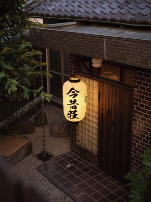 Ein traditionelles japanisches Gebäude mit einem Ziegeldach, einer Holztür und einem Laternenlicht mit japanischen Schriftzeichen.