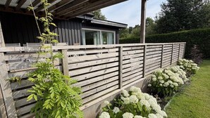 A modern house with a wooden deck, a covered porch, and a well-maintained garden with white flowers.