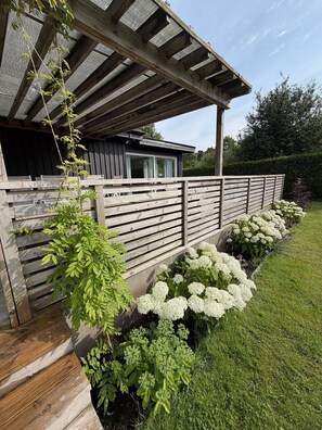 A modern house with a wooden deck, a covered porch, and a well-maintained garden with white flowers.