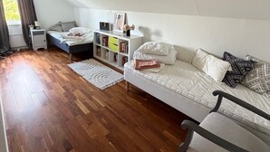 A bedroom with a loft bed, a bedside table, a nightstand, a bookshelf, and a window with curtains.
