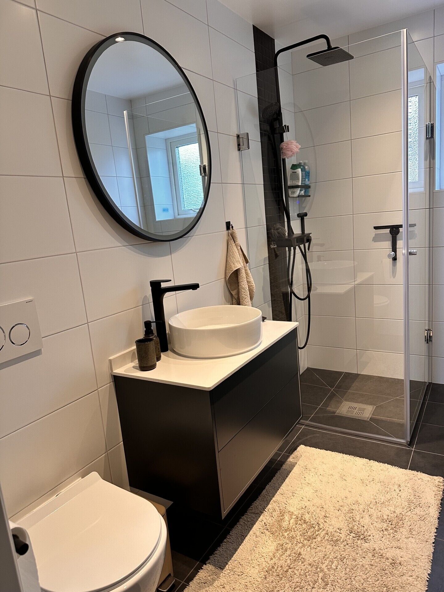 A modern bathroom with a round mirror, a sink, a toilet, and a shower area.