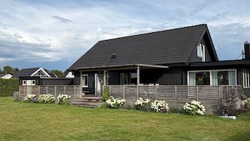 Ein zweistöckiges Haus mit dunklem Dach, einer überdachten Veranda und einem gepflegten Rasen.