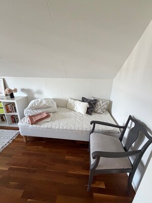 A loft-style bedroom with a white bed, a gray chair, and a bookshelf.