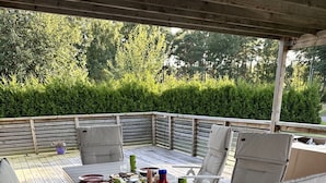 An outdoor dining area with a wooden deck, metal-framed chairs, and a table set for a meal.