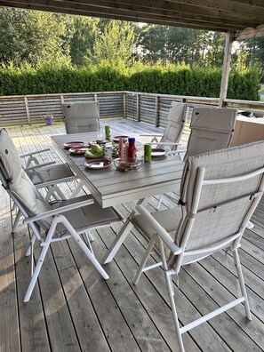 An outdoor dining area with a wooden deck, metal-framed chairs, and a table set for a meal.