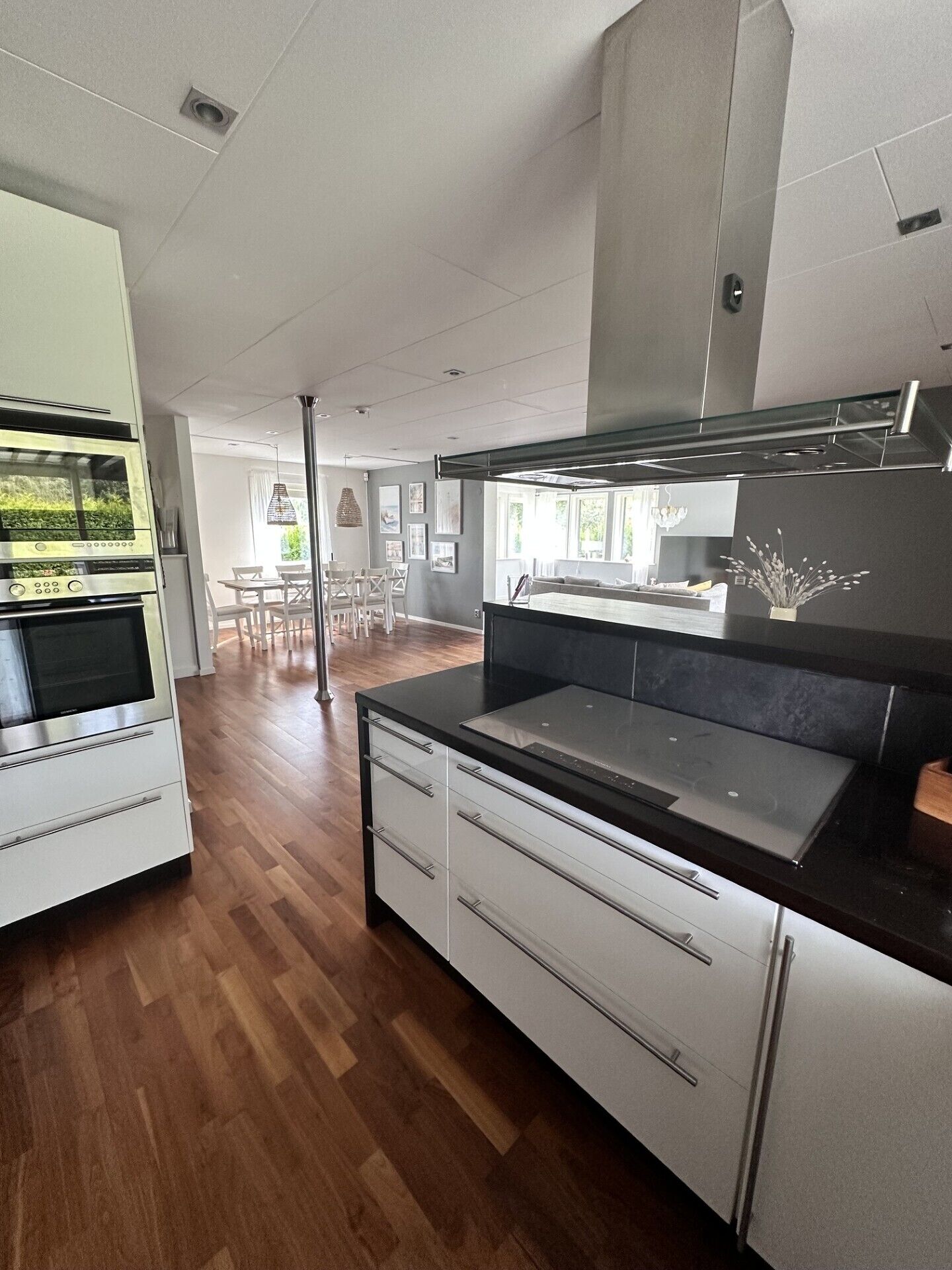 A modern kitchen with a built-in oven, a large island with a black countertop, and a stainless steel range hood.