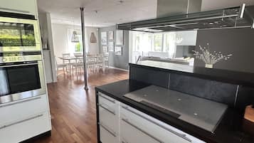 A modern kitchen with a built-in oven, a large island with a black countertop, and a stainless steel range hood.