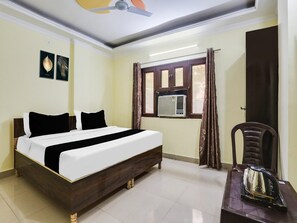 A bedroom with a bed, a chair, a table, an air conditioning unit, and a window with curtains.