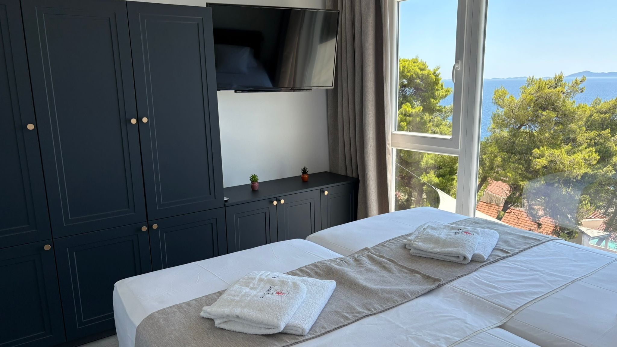 A bedroom with a bed, a TV, and a view of trees and water.
