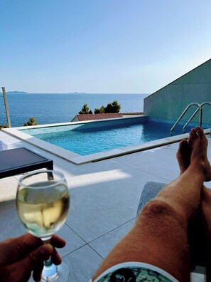 A poolside view with a clear sky, a pool, and a distant view of the sea.